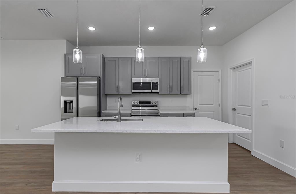 A modern kitchen features gray cabinets, stainless steel appliances, and a large white quartz island — 13177 SW 67TH AVENUE, OCALA, FL