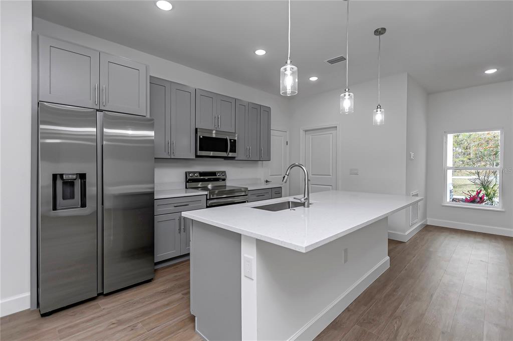 A modern kitchen features gray cabinets, stainless steel appliances, and a white quartz island countertop — 13177 SW 67TH AVENUE, OCALA, FL