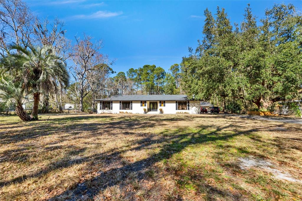 A single-story white house sits on a large, grassy lot surrounded by mature trees — 7569 PARK CITY DRIVE, JACKSONVILLE, FL