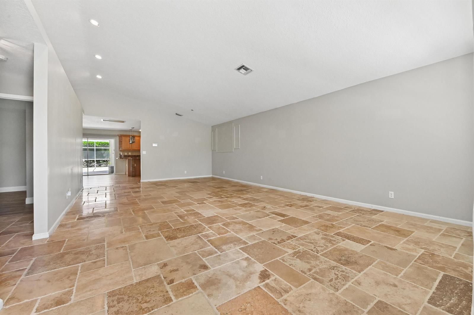 An empty living room features light gray walls, a vaulted ceiling, and tan stone flooring — 1163 Peninsula Way, FL 33413, FL