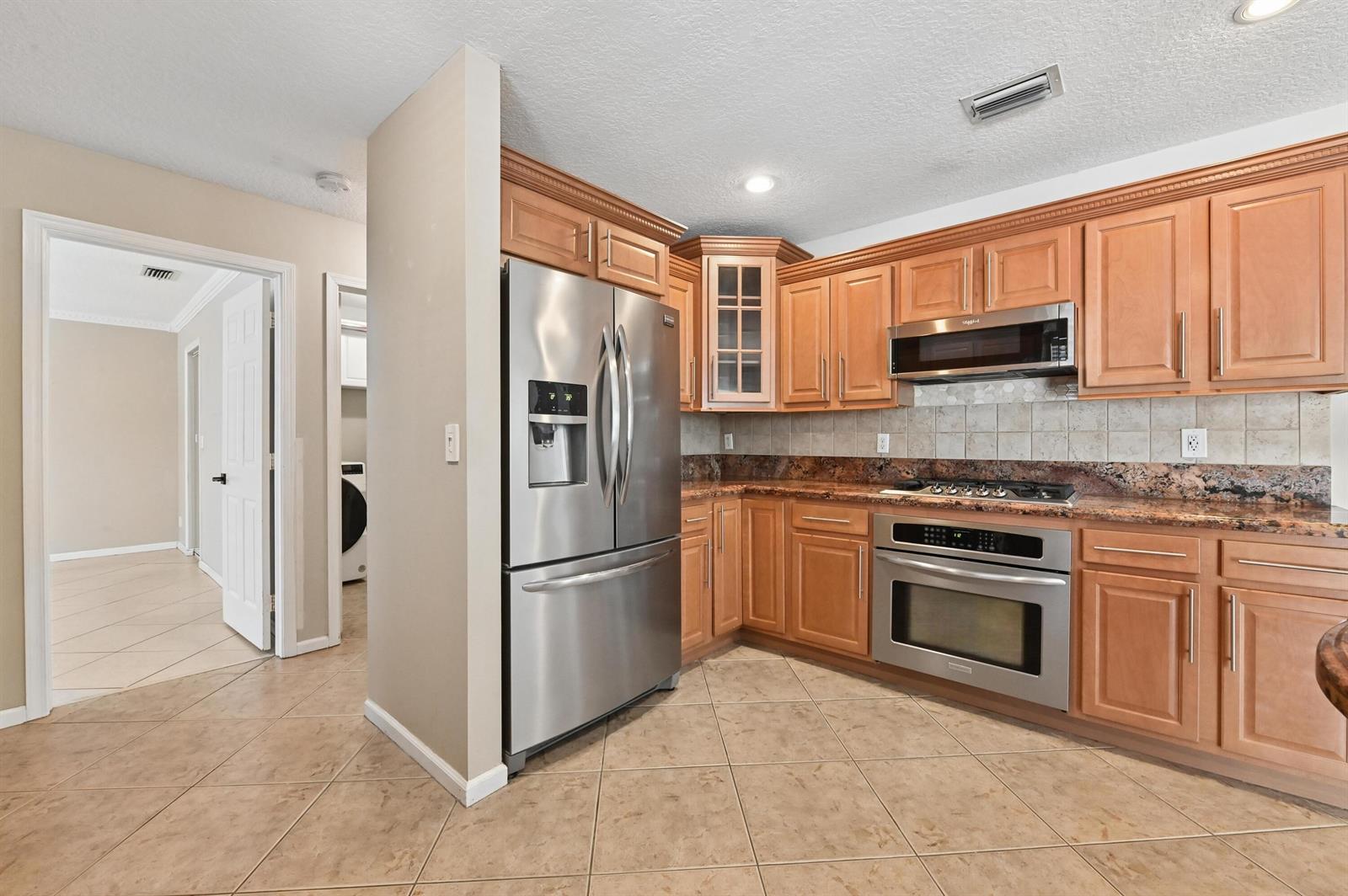 A kitchen features light wood cabinets, stainless steel appliances, and brown granite countertops — 1163 Peninsula Way, FL 33413, FL