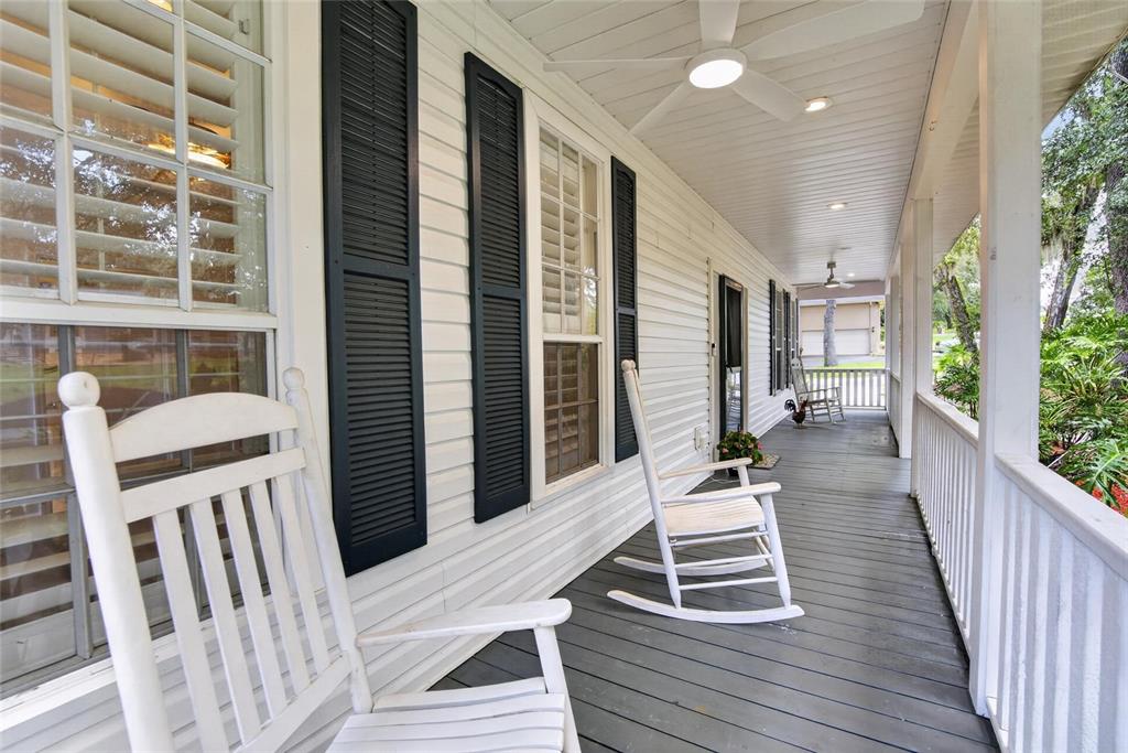 A covered porch features white siding, black shutters, wooden decking, and several white rocking chairs — 1701 COTTAGE OAKS COURT, BRANDON, FL