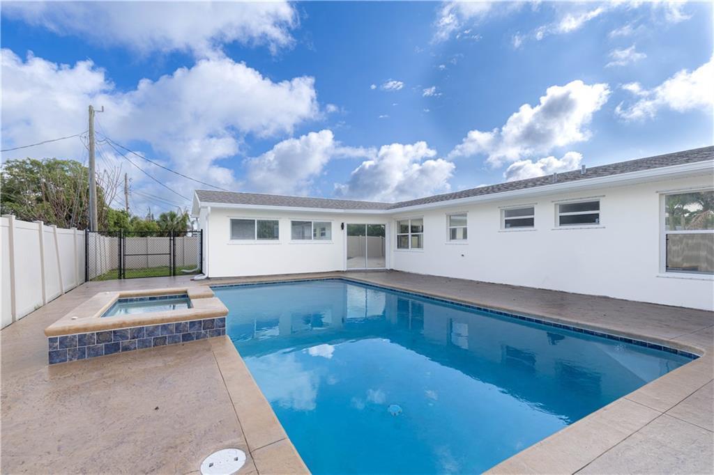 A backyard swimming pool with an attached spa sits beside a white house — SEBASTIAN, FL