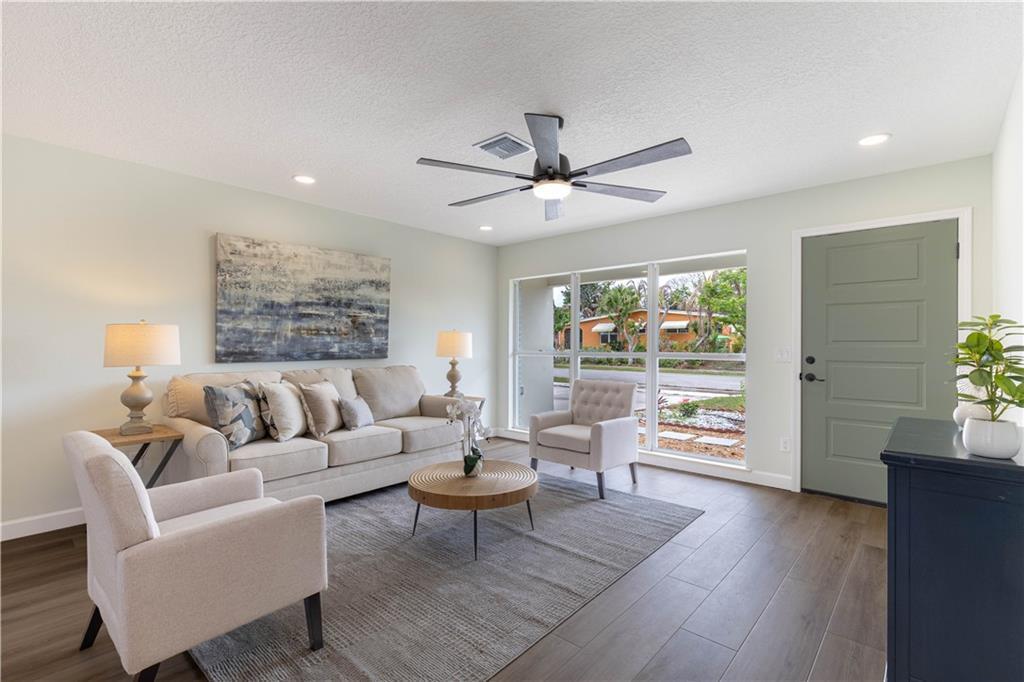 A living room features light walls, wood-look flooring, a beige sofa, and a green door — SEBASTIAN, FL