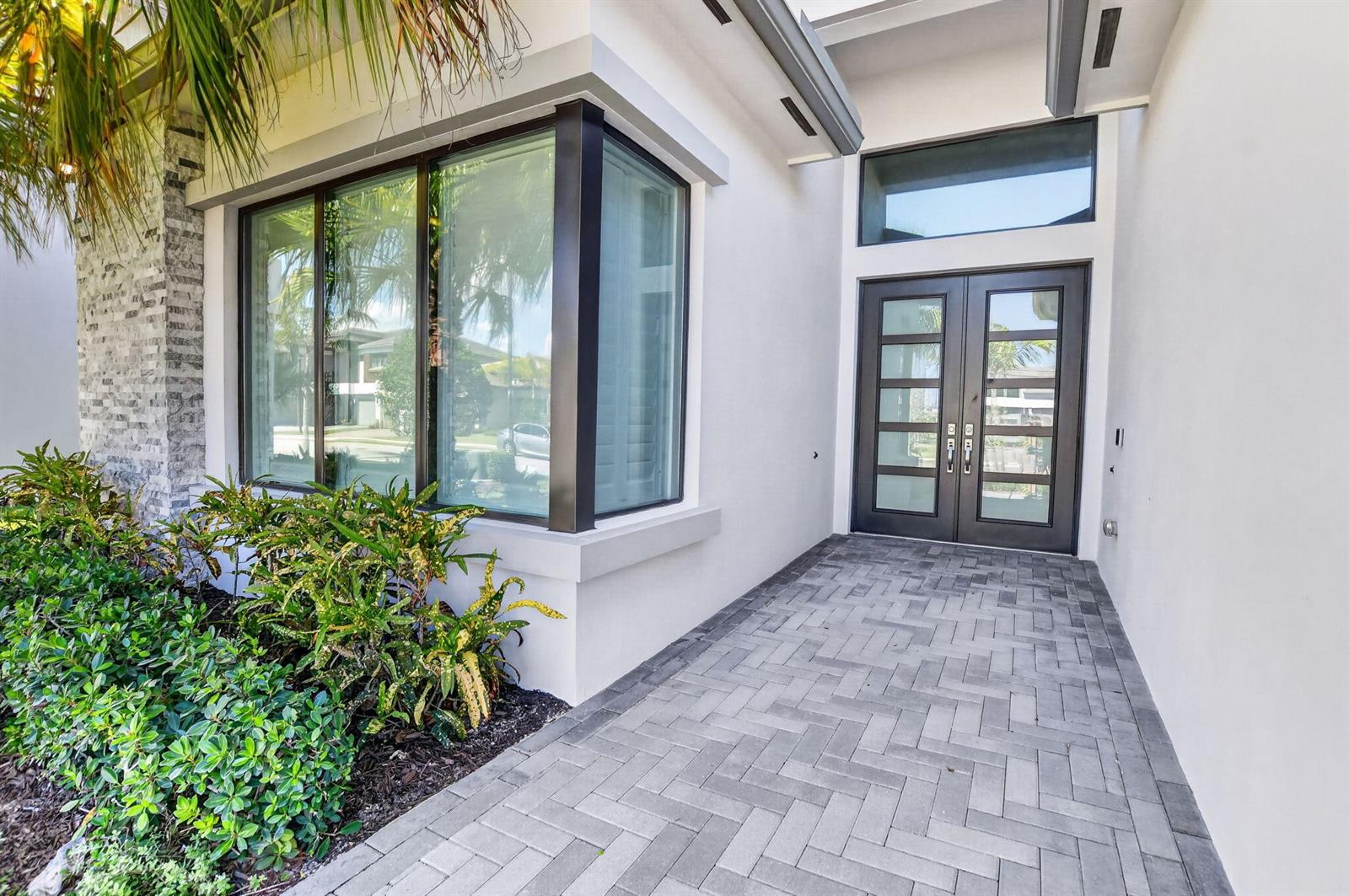 A modern home entrance features a double glass door, a bay window, and stone pavers — 20041 Pacific Dunes Drive, Boca Raton FL 33434, BOCA RATON, FL