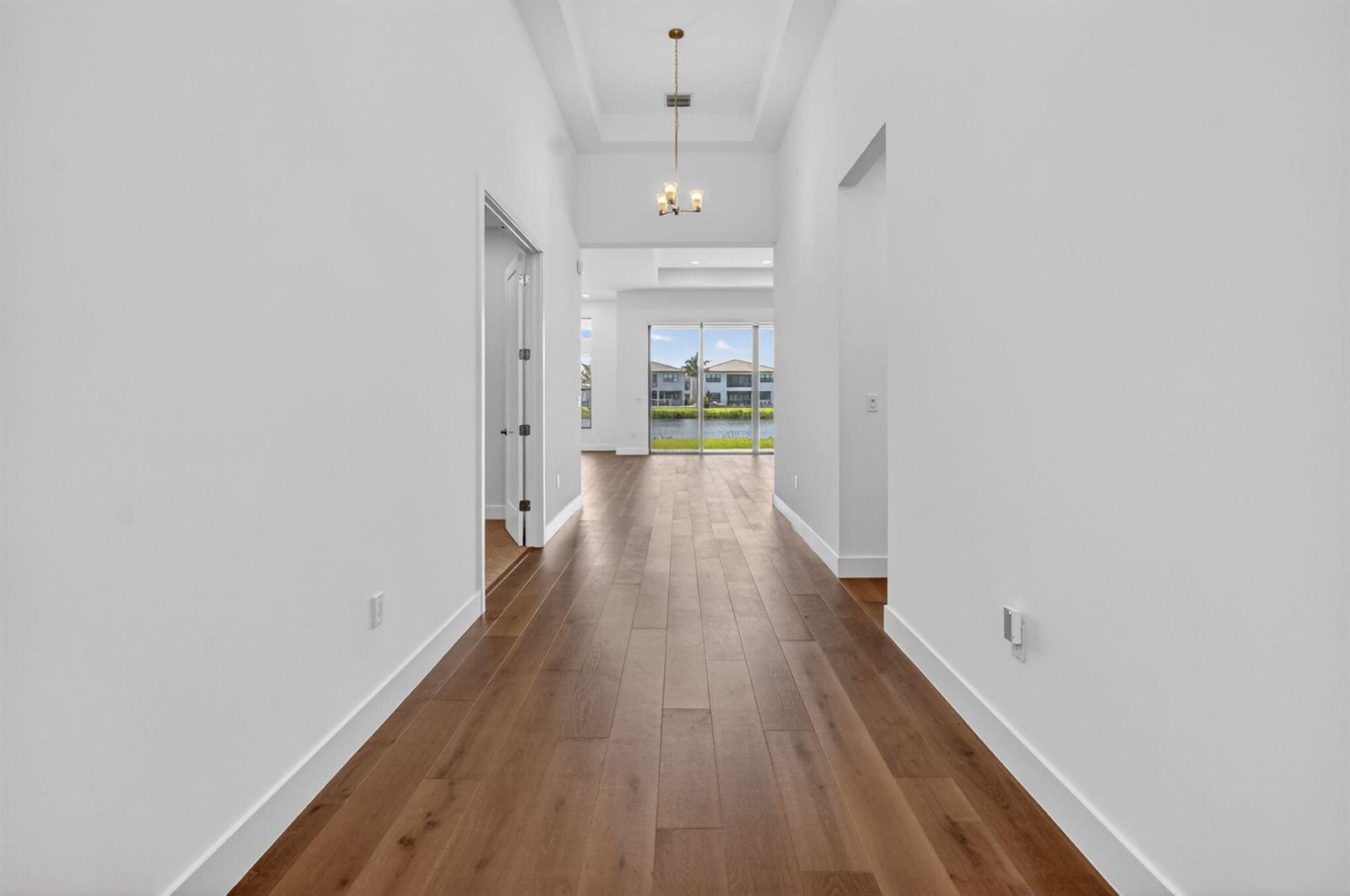A hallway with white walls and wood flooring leads to a room with glass doors — 20041 Pacific Dunes Drive, Boca Raton FL 33434, BOCA RATON, FL