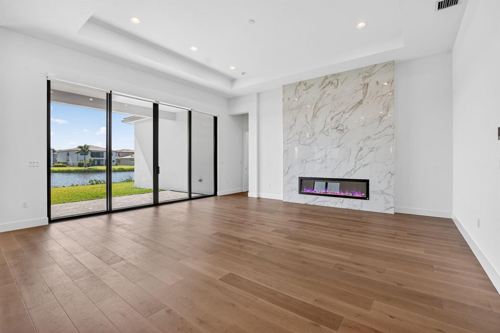 A living room with wood floors, a marble fireplace, and sliding glass doors overlooking water — 20041 Pacific Dunes Drive, Boca Raton FL 33434, BOCA RATON, FL