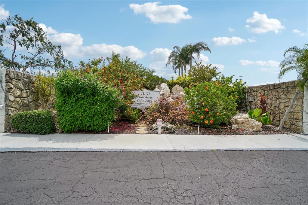 A stone wall borders a landscaped garden with a condominium sign and flowering bushes — 1601 43RD STREET N UNIT 224, ST PETERSBURG, FL