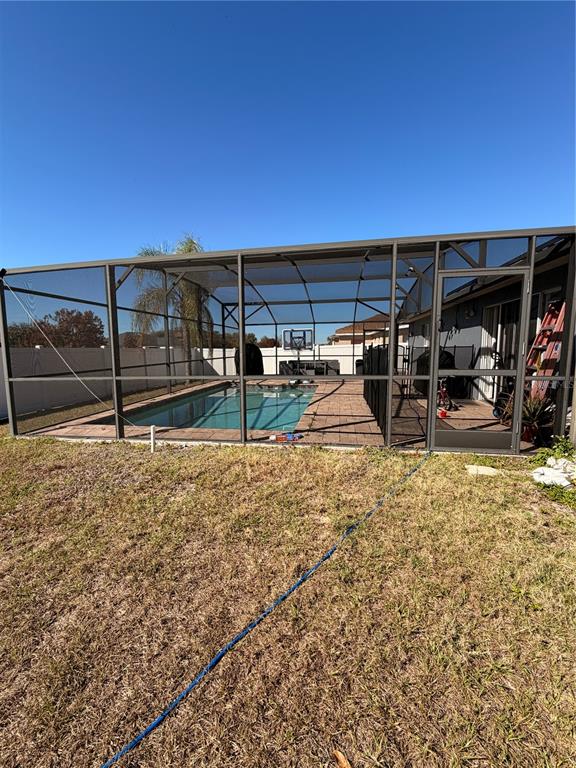 A screened-in swimming pool enclosure sits in a backyard with a blue hose on grass — 436 BLOOMFIELD DRIVE, KISSIMMEE, FL