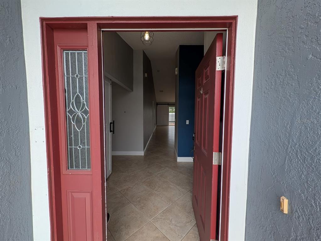 An open red front door reveals a tiled entryway leading to a long interior hallway — 436 BLOOMFIELD DRIVE, KISSIMMEE, FL