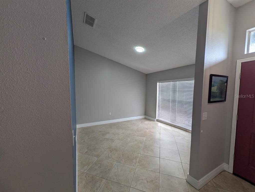 An empty room with light gray walls, tile flooring, and a large window with blinds — 436 BLOOMFIELD DRIVE, KISSIMMEE, FL
