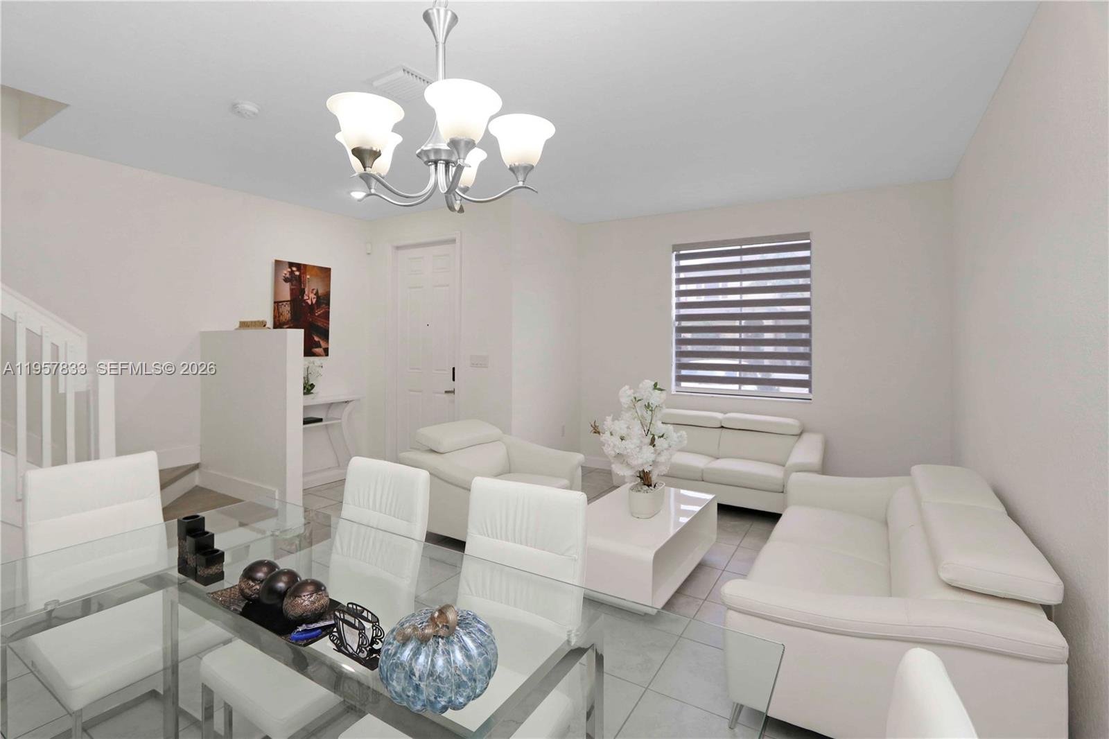 This open-concept living and dining area features white furniture, tile flooring, and a chandelier — 10628 W 33rd Way, Hialeah FL 33018, HIALEAH, FL