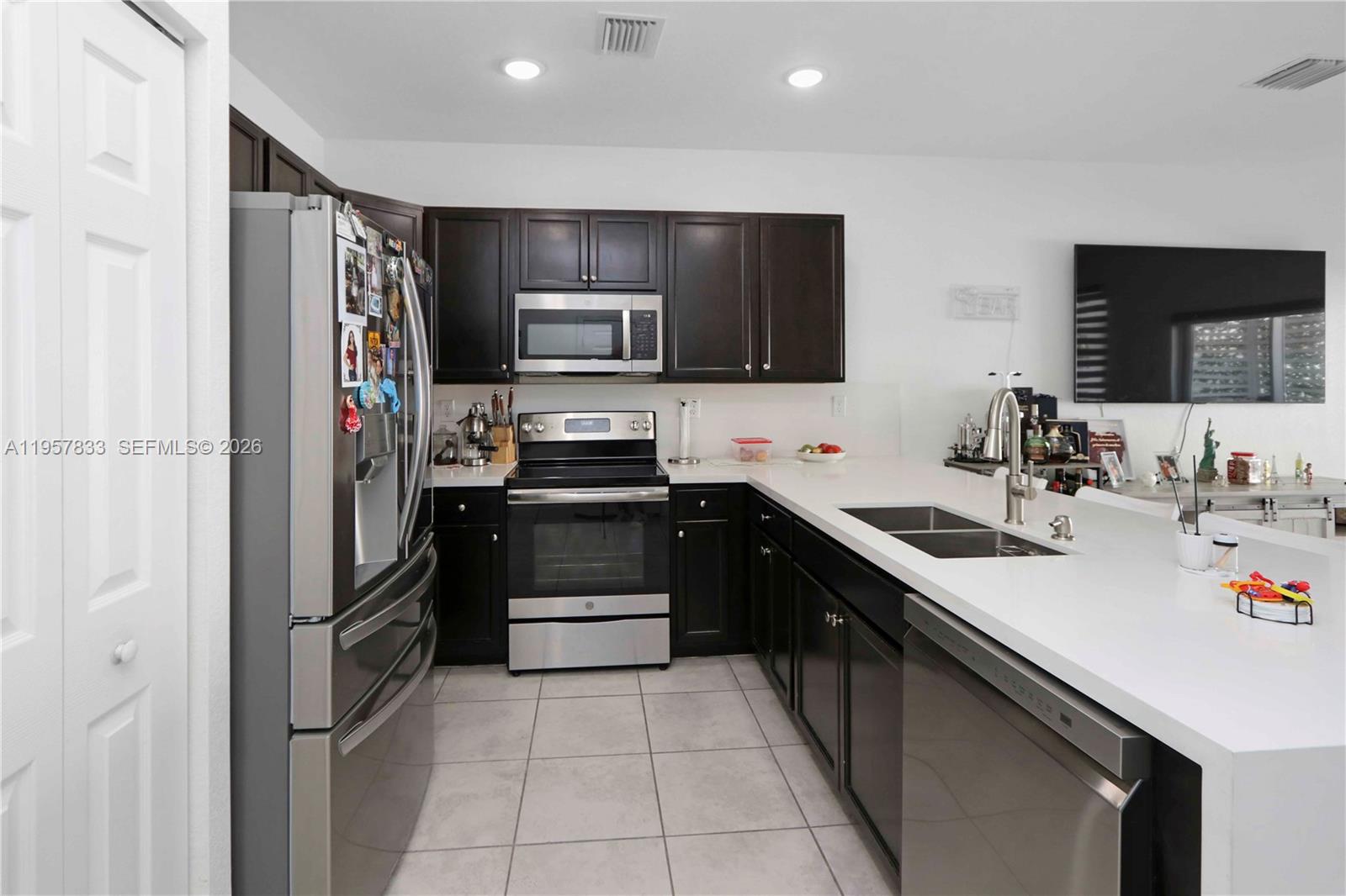 A kitchen features dark wood cabinets, stainless steel appliances, and white countertops — 10628 W 33rd Way, Hialeah FL 33018, HIALEAH, FL