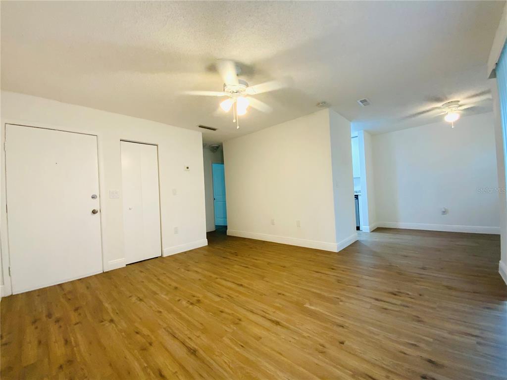 An empty living room features wood-look flooring, white walls, and two ceiling fans — 305 E WELLINGTON COURT UNIT 62, TAMPA, FL