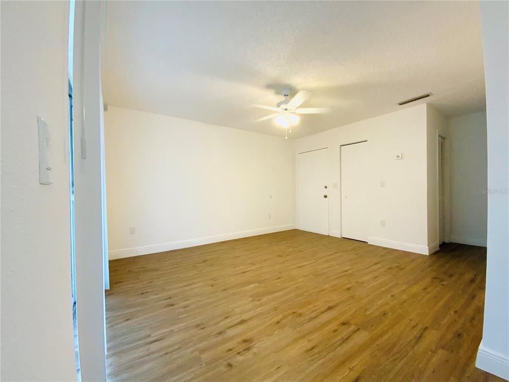 An empty room features white walls, a ceiling fan, and light wood-look flooring — 305 E WELLINGTON COURT UNIT 62, TAMPA, FL