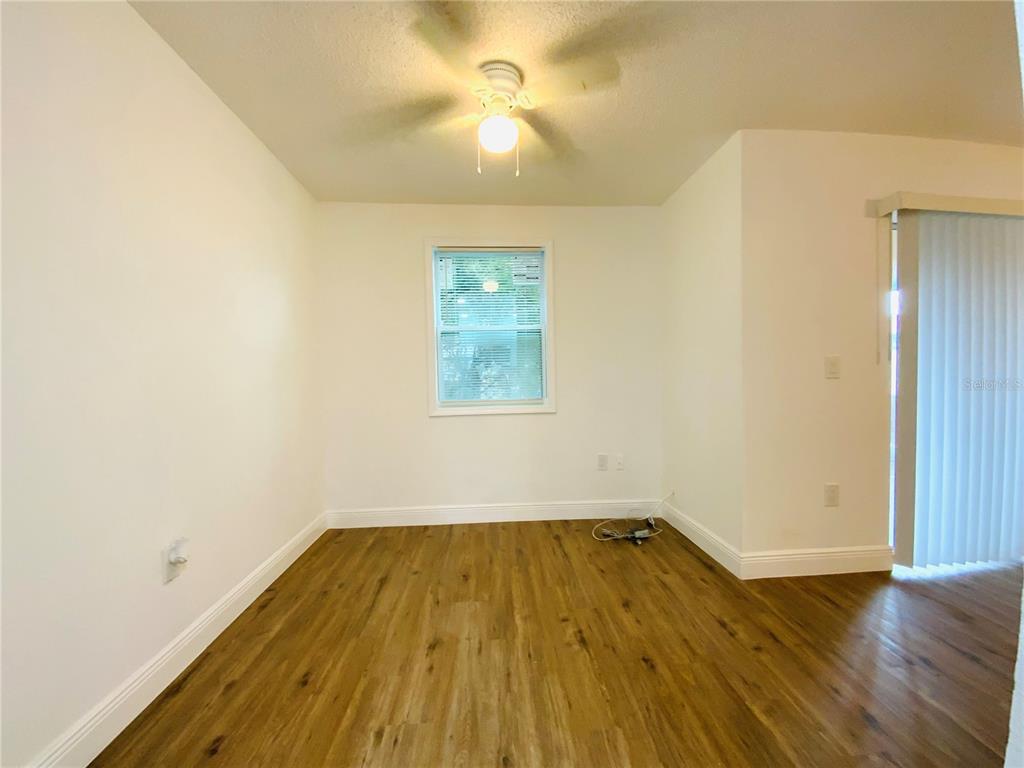 An empty room features wood-look flooring, white walls, a ceiling fan, and a sliding glass door — 305 E WELLINGTON COURT UNIT 62, TAMPA, FL