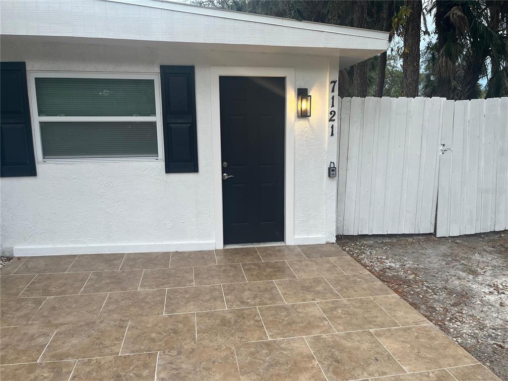 A white exterior wall with a black door, a window, and a tiled patio — 7119-7121 OAKWOOD, NEW PORT RICHEY, FL