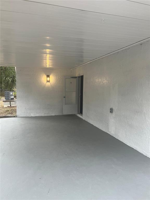 A covered carport with a gray concrete floor, white walls, and a single exterior door — 7119-7121 OAKWOOD, NEW PORT RICHEY, FL