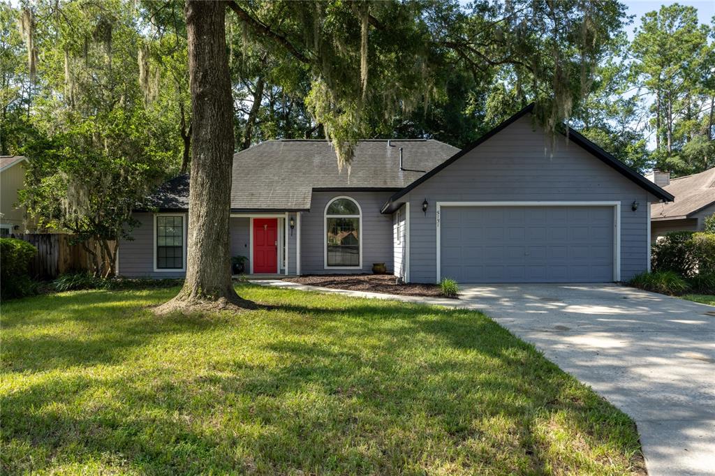 A gray single-story house with a red front door, a two-car garage, and large trees — 5131 NW 35TH PLACE, GAINESVILLE, FL