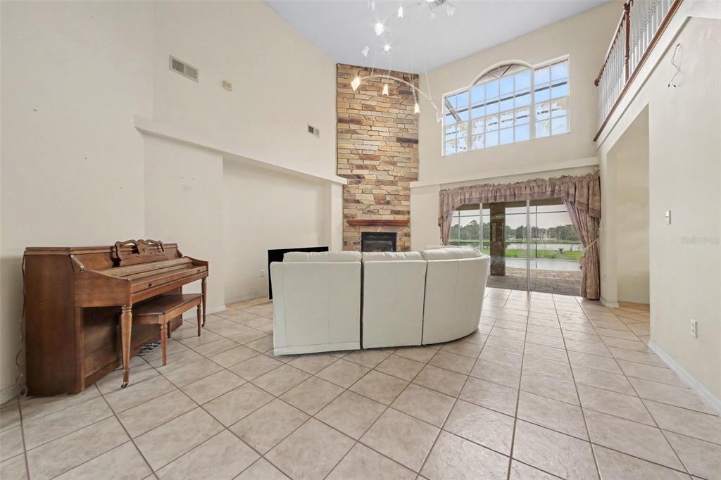 A spacious living room with a stone fireplace, tile floors, a piano, and large windows — 19112 ORTEGA STREET, ORLANDO, FL