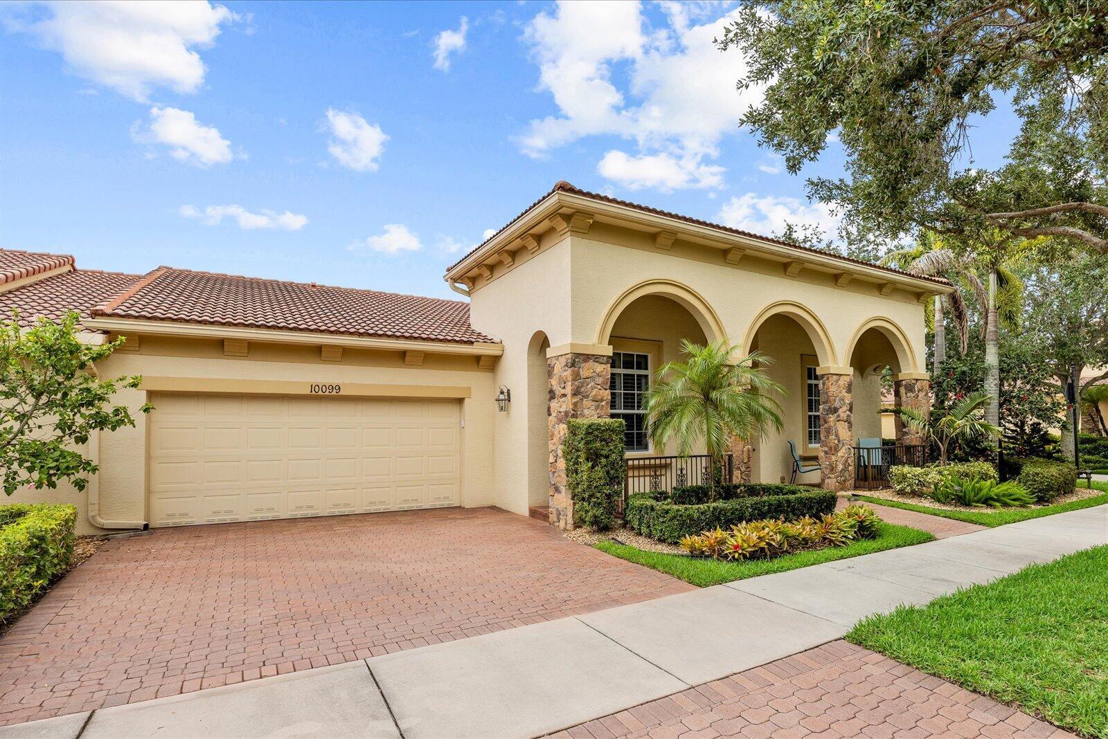 A single-story house with a beige stucco exterior, stone accents, arched entryway, and brick driveway — 10099 SW Duccio Lane, FL 34986, FL