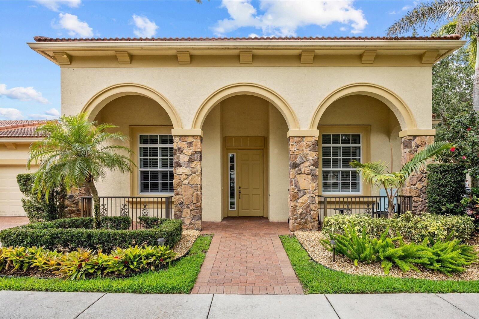 A tan stucco house features three arched entryways, stone pillars, and a brick walkway — 10099 SW Duccio Lane, FL 34986, FL