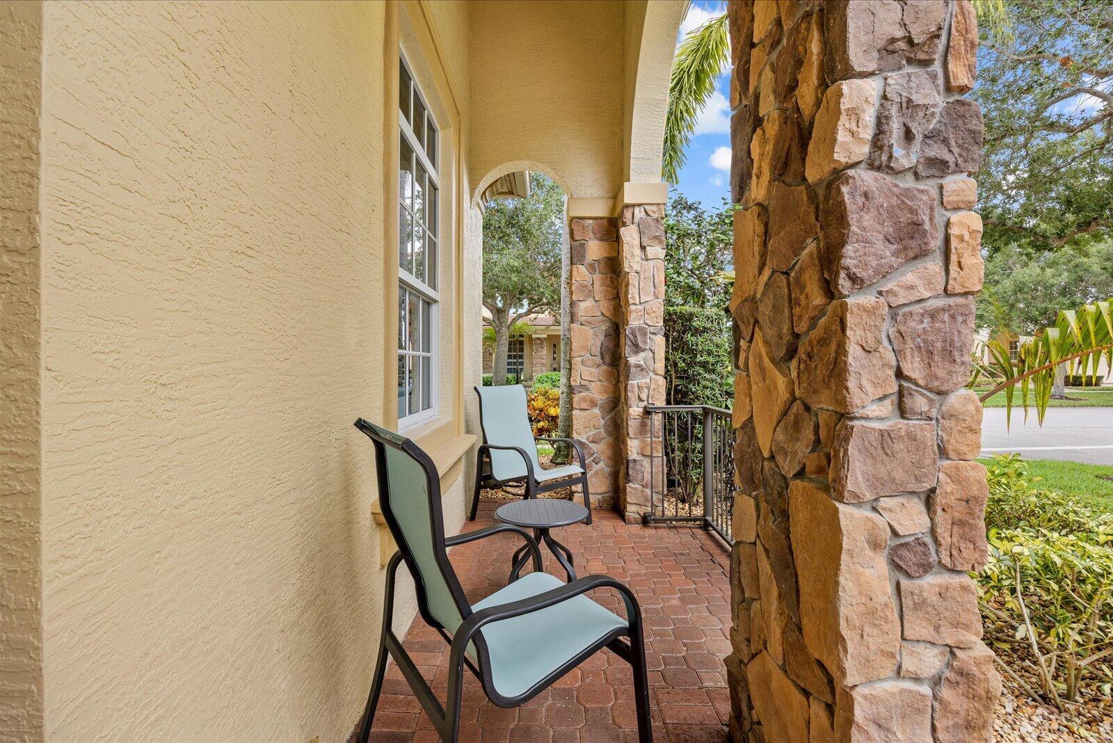 A covered brick patio features two chairs, a small table, and stone-clad support columns — 10099 SW Duccio Lane, FL 34986, FL
