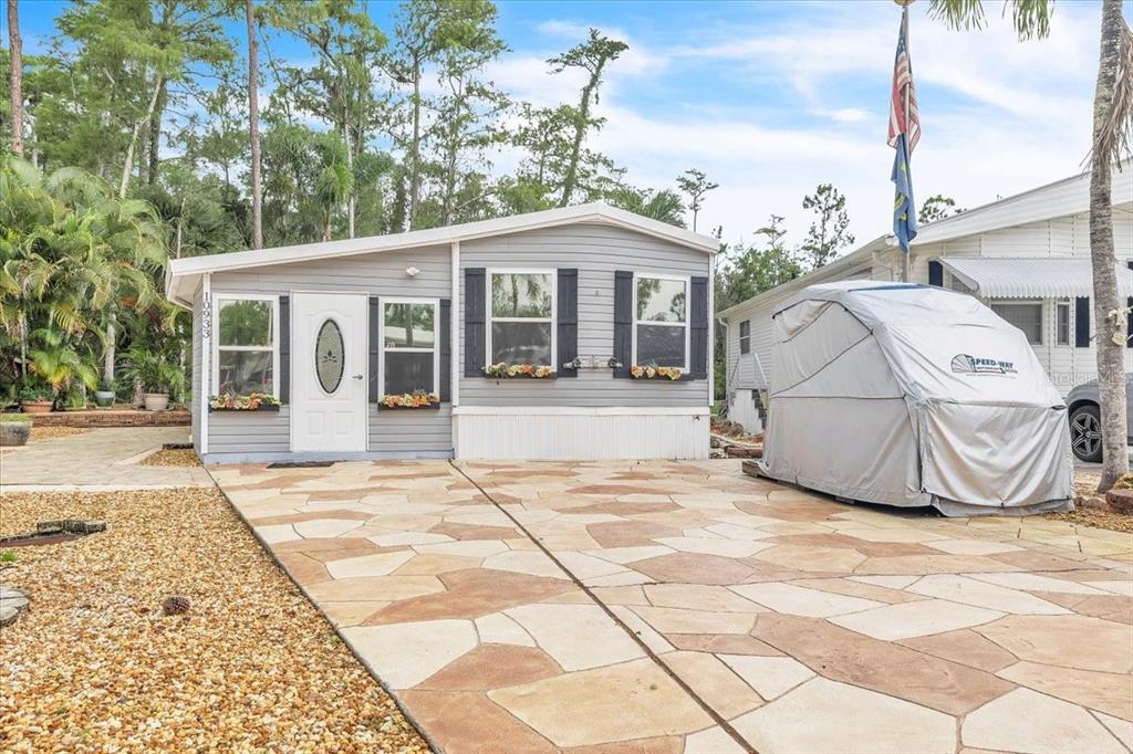 A gray manufactured home with a flag pole and a covered motorcycle parked outside — 10933 BROWN PELICAN CIRCLE, ESTERO, FL