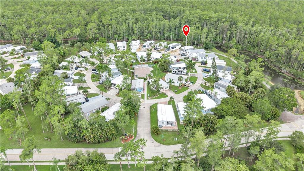 An aerial view shows a residential community of manufactured homes surrounded by dense green trees — 10933 BROWN PELICAN CIRCLE, ESTERO, FL
