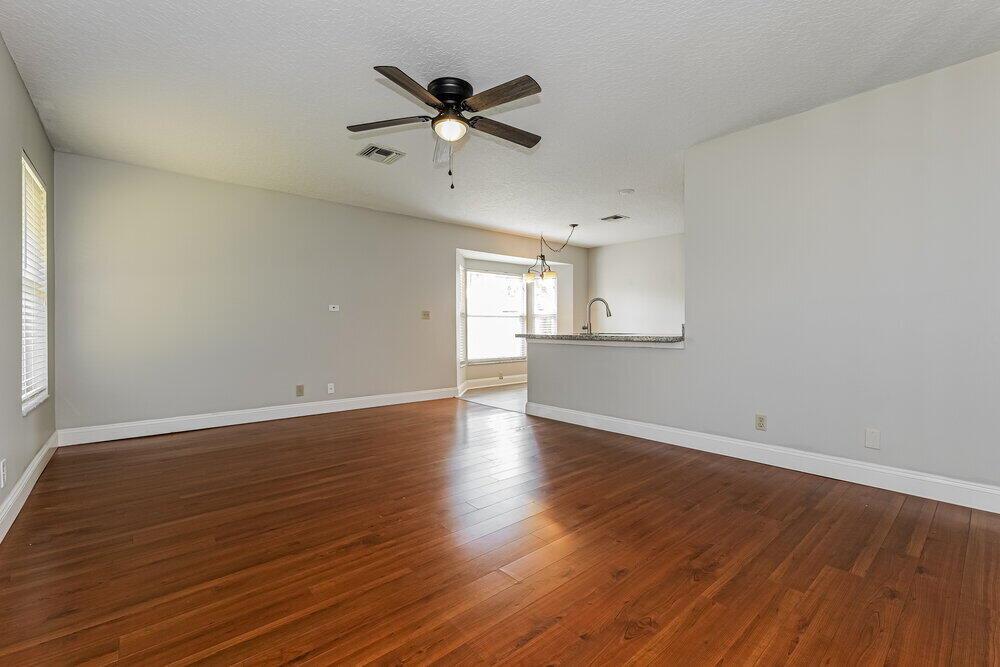 An empty living room with hardwood floors, a ceiling fan, and an open kitchen area — WELLINGTON, FL