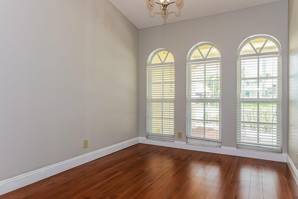 An empty room with hardwood floors, light gray walls, and three arched windows with blinds — WELLINGTON, FL