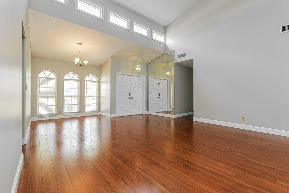 An empty living room features hardwood floors, vaulted ceilings, arched windows, and mirrored wall panels — WELLINGTON, FL