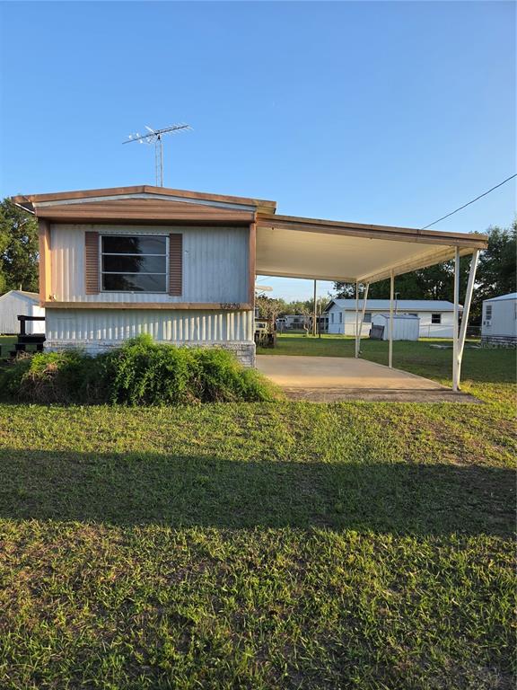 A single-story mobile home with a metal roof, attached carport, and a large front bush — 17420 SE 36TH LANE, OCKLAWAHA, FL