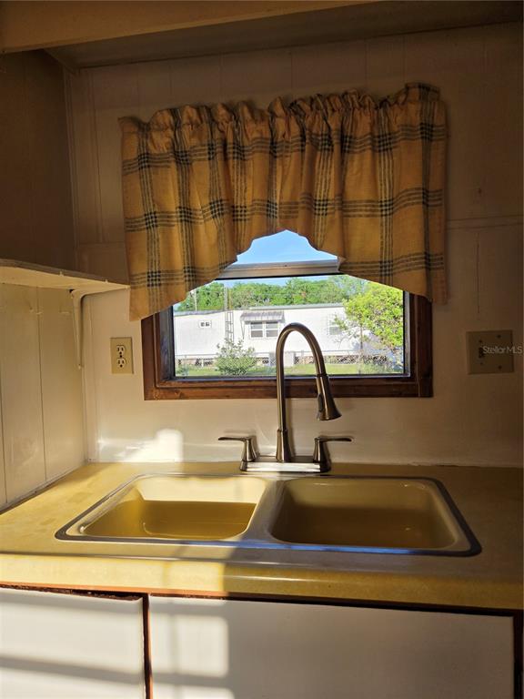 A kitchen sink with a modern faucet sits beneath a window with plaid curtains — 17420 SE 36TH LANE, OCKLAWAHA, FL