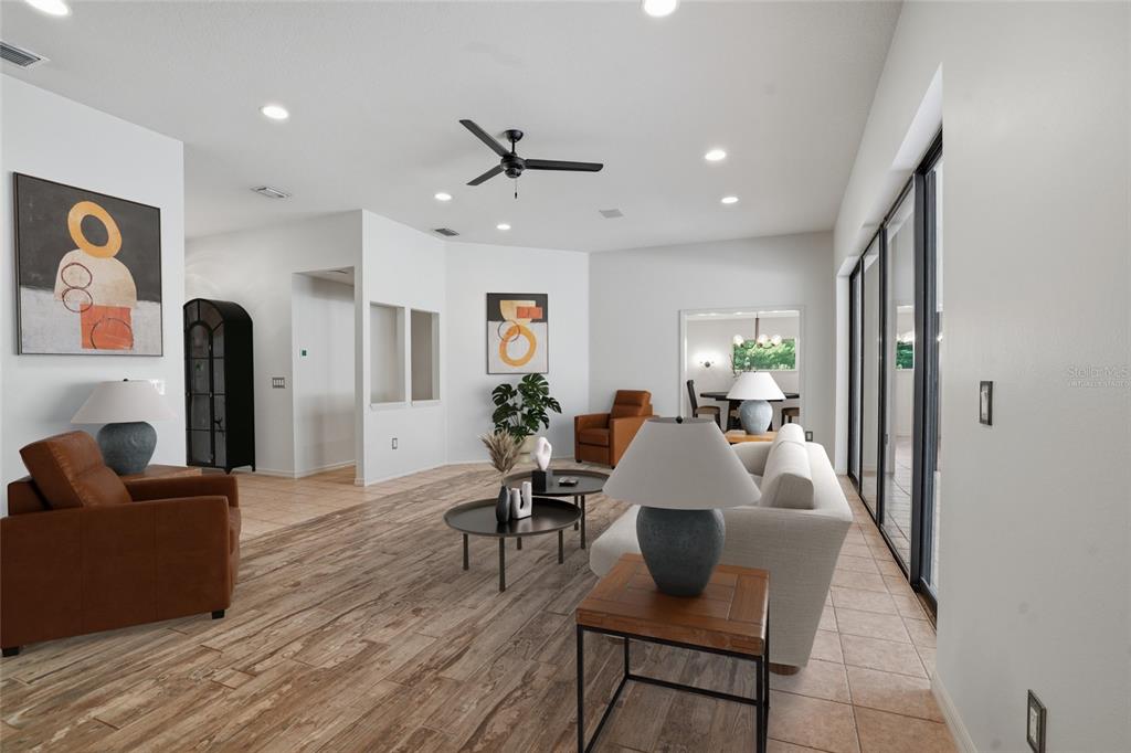 A living room features wood-look tile flooring, white walls, a ceiling fan, and sliding glass doors — 9020 SHENANDOAH RUN, WESLEY CHAPEL, FL