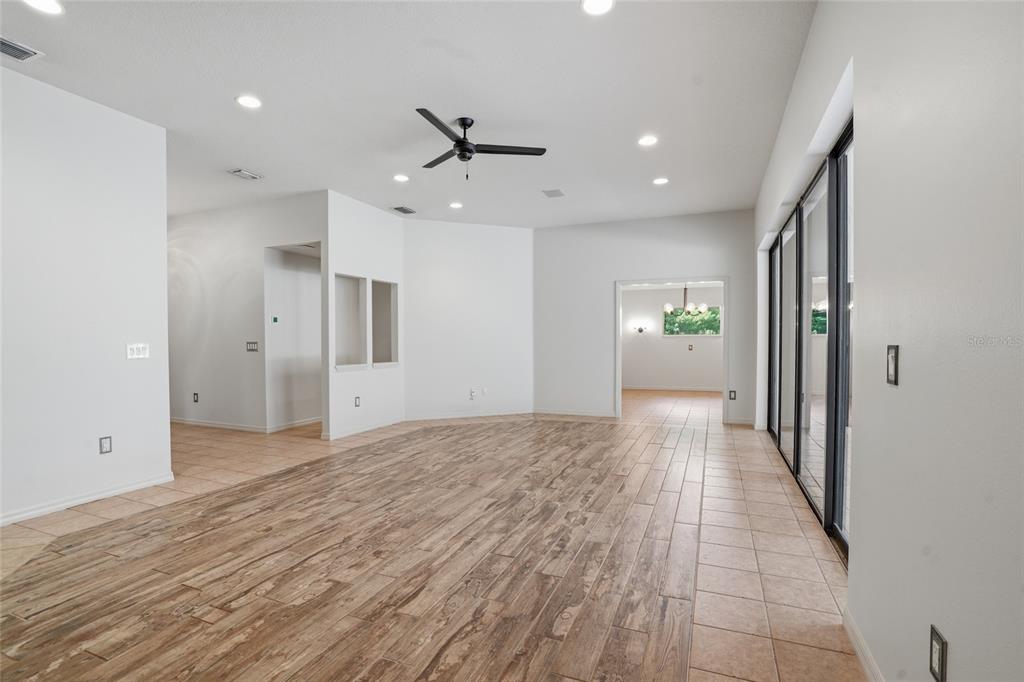 A spacious living room features wood-look tile flooring, a ceiling fan, and large sliding glass doors — 9020 SHENANDOAH RUN, WESLEY CHAPEL, FL