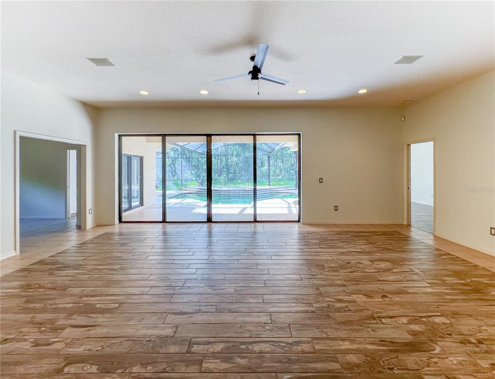 A spacious living room features wood-look tile flooring, a ceiling fan, and large sliding glass doors — 9020 SHENANDOAH RUN, WESLEY CHAPEL, FL
