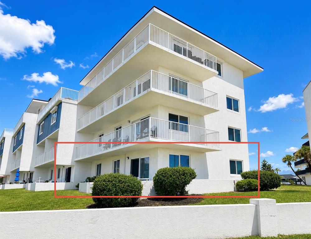 The ground floor of a white multi-story apartment building features a patio and landscaping — 3510 S OCEAN SHORE BOULEVARD UNIT 112, FLAGLER BEACH, FL