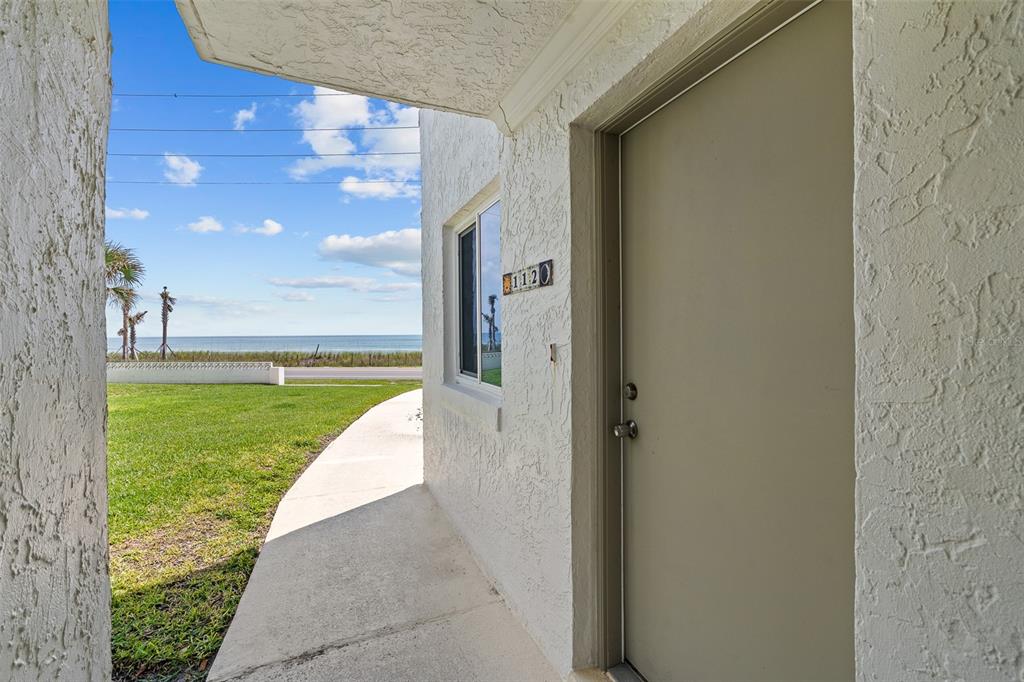 A view from a covered entryway looking out toward a grassy lawn and the ocean — 3510 S OCEAN SHORE BOULEVARD UNIT 112, FLAGLER BEACH, FL