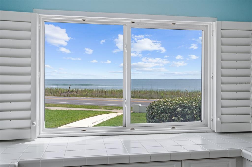A white-tiled kitchen counter sits before a window with shutters overlooking a coastal road — 3510 S OCEAN SHORE BOULEVARD UNIT 112, FLAGLER BEACH, FL