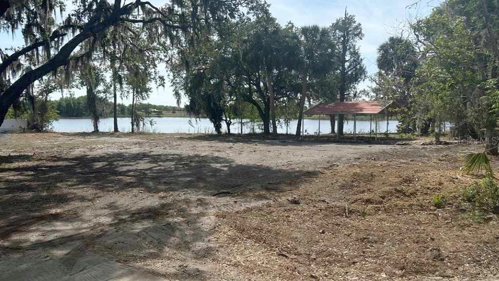 A cleared, sandy lot features mature trees and a small covered structure near a lake — 233 RONALD REAGAN PARKWAY, DAVENPORT, FL