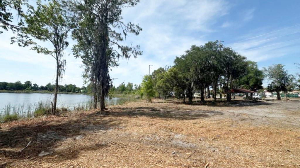 A vacant, grassy lot sits beside a lake with several large trees on the property — 233 RONALD REAGAN PARKWAY, DAVENPORT, FL