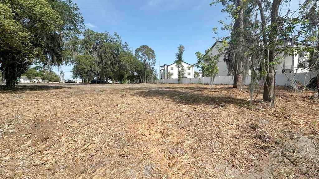 A cleared, flat lot with scattered trees and a white fence near apartment buildings — 233 RONALD REAGAN PARKWAY, DAVENPORT, FL