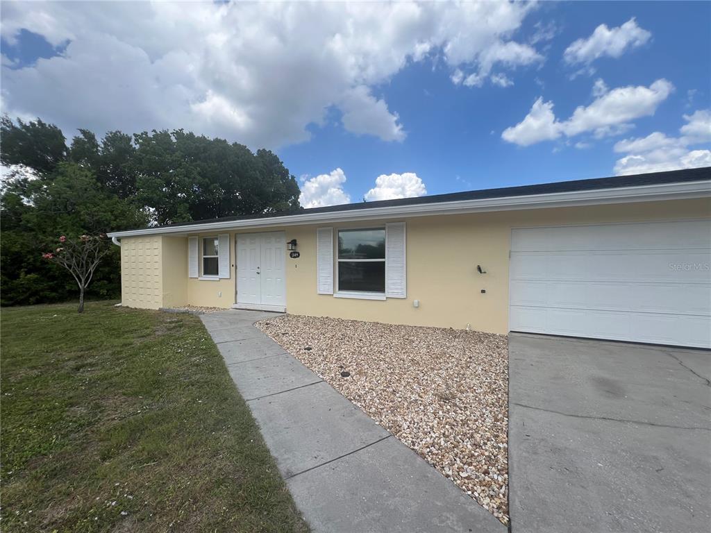 A single-story house with yellow siding, white shutters, a gravel front yard, and a garage — 249 SEMINOLE BOULEVARD NW, PORT CHARLOTTE, FL