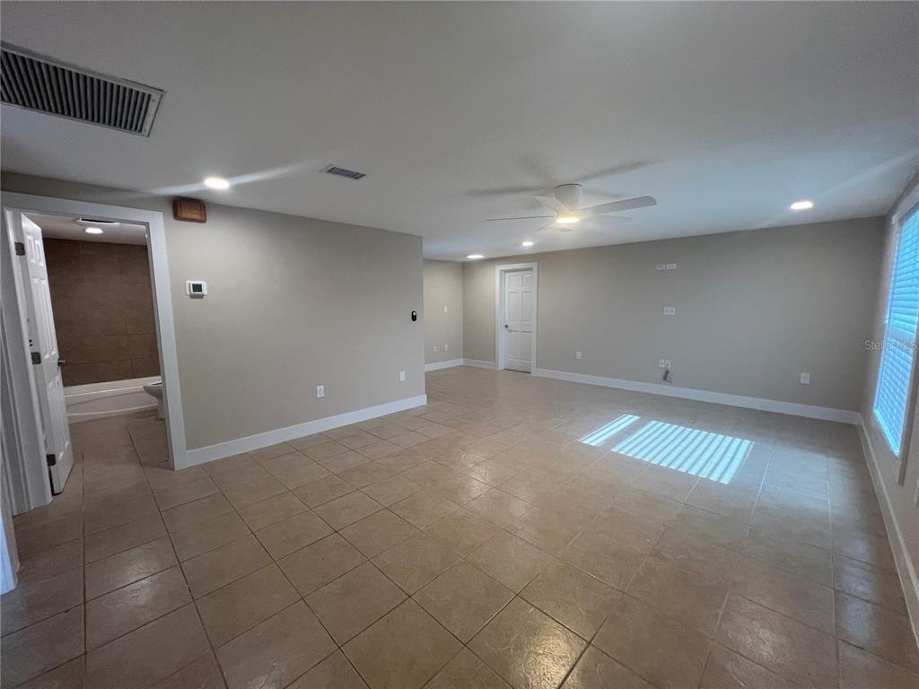 A spacious room with beige tile flooring, a ceiling fan, and an adjacent bathroom — 249 SEMINOLE BOULEVARD NW, PORT CHARLOTTE, FL