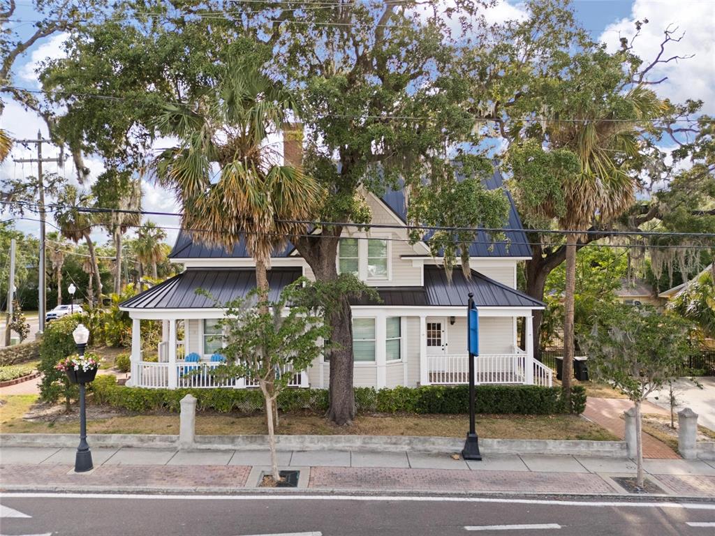 A two-story house with a metal roof and a wrap-around porch sits behind trees — 4 W ORANGE STREET, TARPON SPRINGS, FL