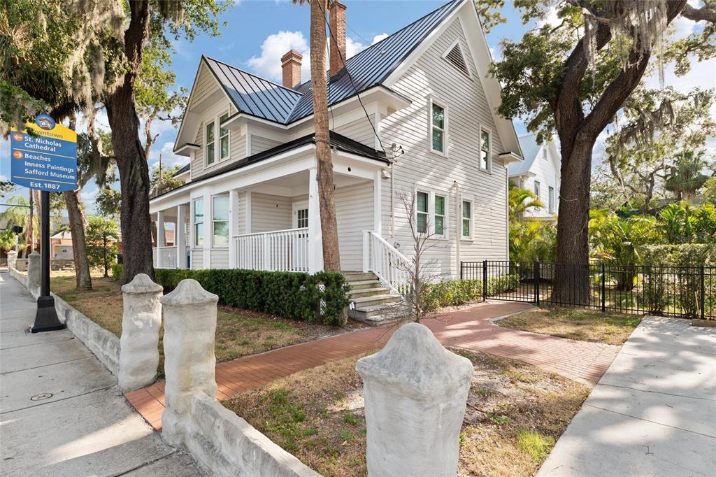 A two-story white house with a metal roof and a front porch sits behind stone pillars — 4 W ORANGE STREET, TARPON SPRINGS, FL