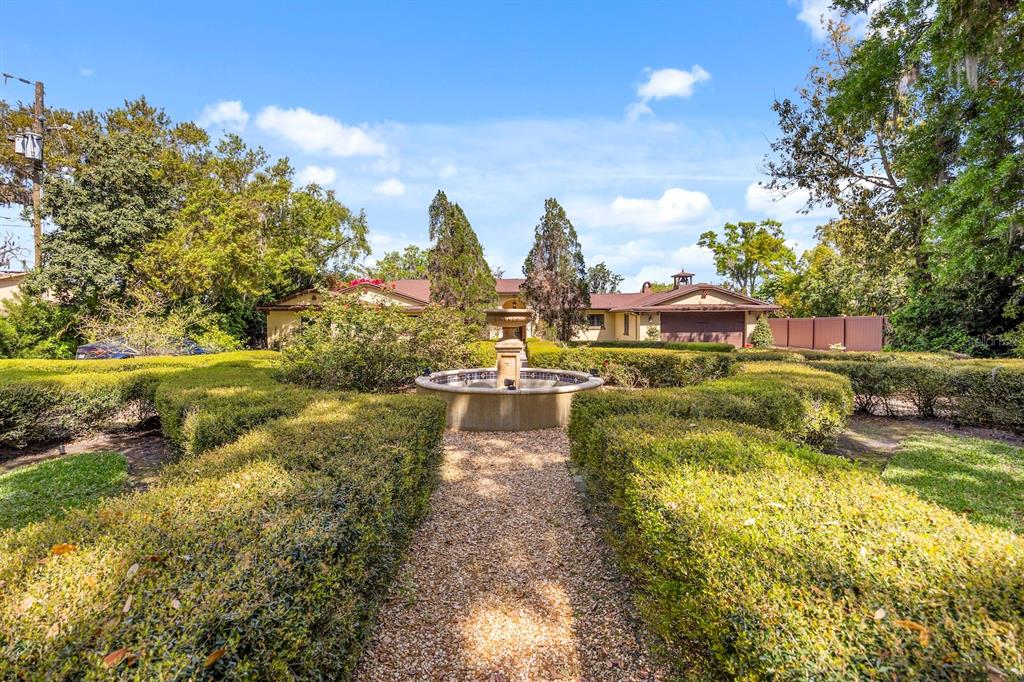 A gravel path leads through a manicured hedge garden to a fountain in front of a house — 5400 KENMORE LANE, ORLANDO, FL