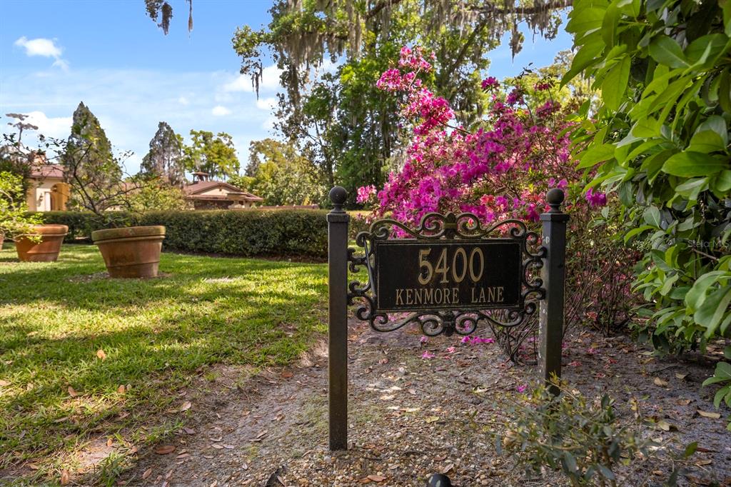 A metal address sign stands in a garden with pink flowers and large potted plants — 5400 KENMORE LANE, ORLANDO, FL