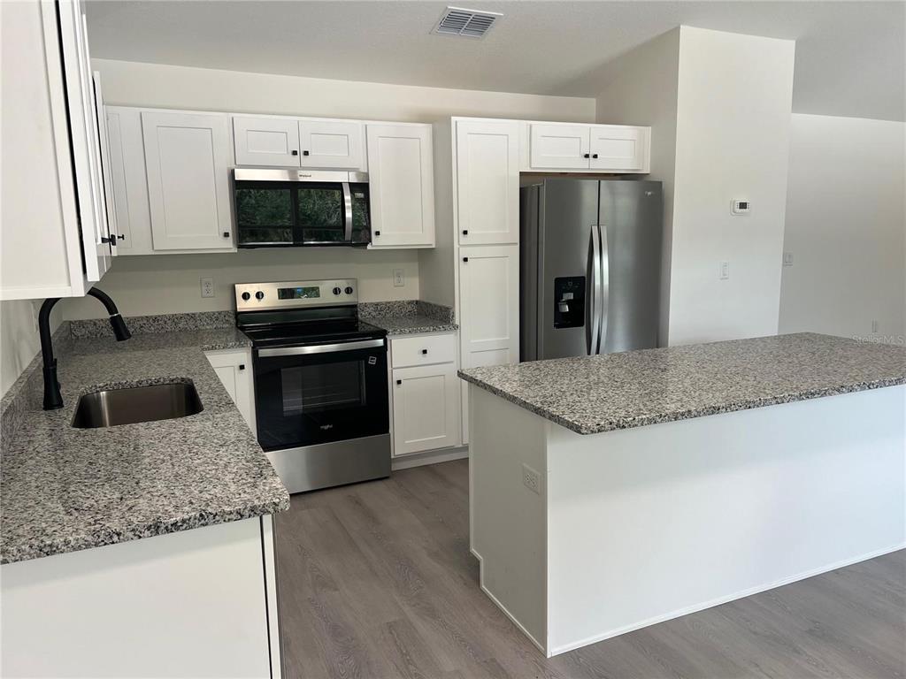 A kitchen features white cabinets, granite countertops, stainless steel appliances, and light wood-look flooring — 14173 SW 60TH TERRACE UNIT 2, OCALA, FL
